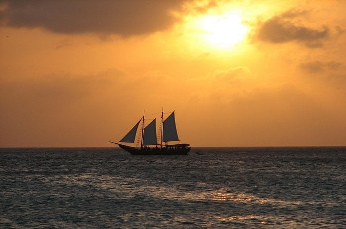 Silhouette of a three-masted sailing ship on the ocean at sunset with golden sky