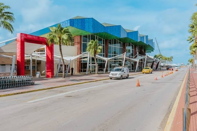 Modern building with blue curved roof and red entrance frame on a wide street with palm trees and parked cars